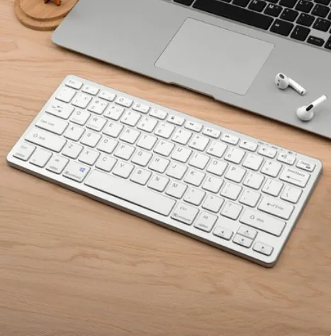 White compact keyboard shown on a desk with laptop and earbuds