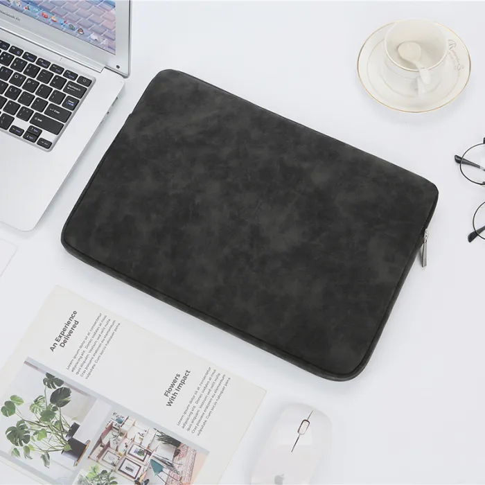 Closed black zippered laptop sleeve shown beside desk accessories